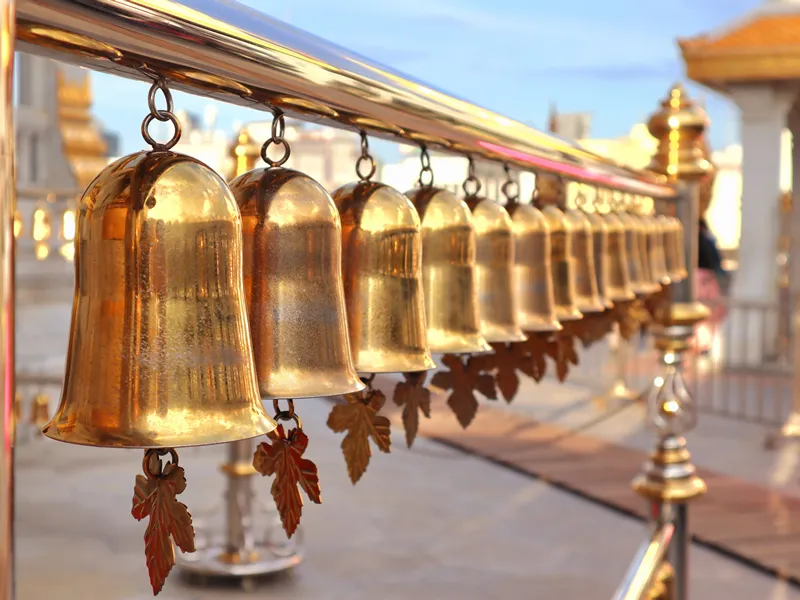 Small bells hanging in a row, glowing golden yellow, found at Wat Traimit Wittayaram Worawihan Temple in Bangkok.